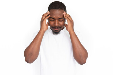 Annoyed young man suffering from headache. Male African American model with closed eyes, short haircut and beard in white T-shirt holding hands at temples because of headache. Pain concept