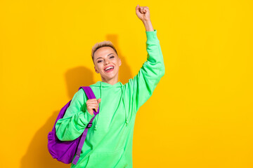 Photo of delighted positive girl raise fist luck accomplishment empty space isolated on yellow color background