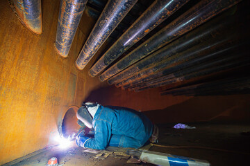 Welding male worker metal is part of machinery plate tank beam pipe construction flash spark inside confined