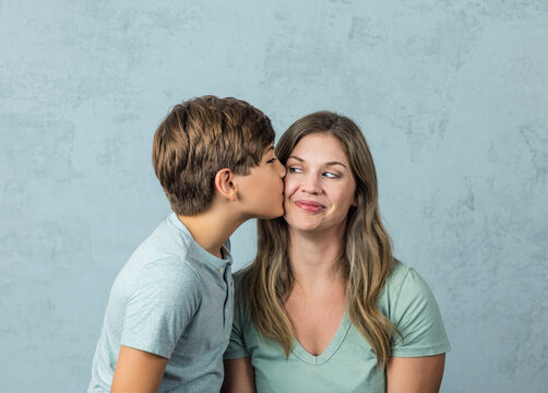 a tween son kissing his mom in her forties on the cheek with a green background