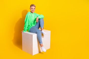 Full size photo of nice cheerful girl sit podium have good mood empty space ad isolated on yellow color background