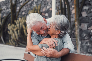 Middle age woman sitting on bench of park with old man hugging her from the back. Couple of retired...