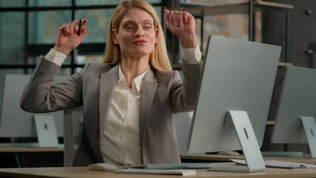 Caucasian middle-aged adult woman dancing listening music at workplace sing song to pen like microphone. Business lady businesswoman entrepreneur worker in office funny dance singing to computer audio