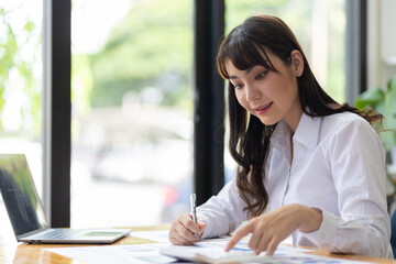 Businesswoman working with financial documents on laptop in office desk.