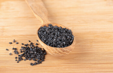 Black natural salt on a wooden spoon and wooden background.