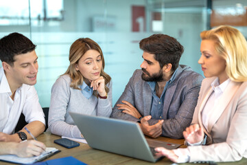 Group of young business people working and communicating while sitting at the office desk together.