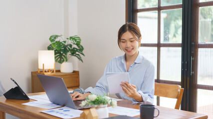 Remote business concept, Businesswoman is reading marketing data in notebook and working on laptop