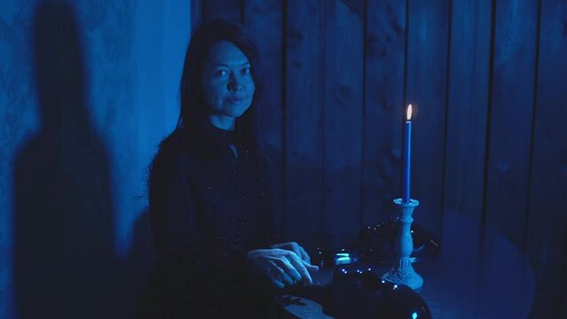 a girl sits at a table with a candle and looks at a black mask. High quality FullHD footage
