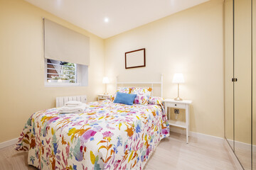 Bedroom with double bed and lined wall with built-in wardrobe with mirror doors and colorful patterned bedspread