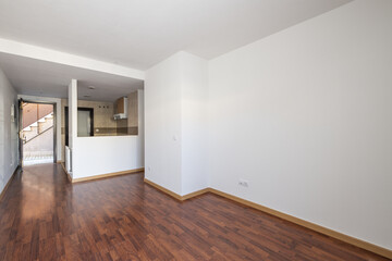 An empty loft-style apartment with a semi-open kitchen with serving hatch and reddish jatoba flooring