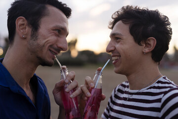 Happy young couple enjoy at the beach. Men drinking juice. LGBT community.