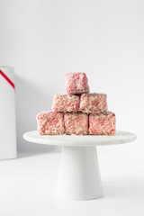 Pink lamingtons on a white marble cake stand   Australian raspberry lamingtons, small cakes covered in desiccated coconuts