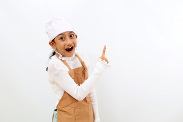 Wow expression of little girl in chef uniform presenting something at blank space. Isolated on white background