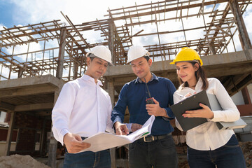 Engineer group and worker meeting, discussion with construction blueprint on site work and point finger to the site workplace. Builders and architects in hardhats with blueprint on construction site