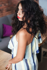 curly sexy brunette poses in the cafe hall; wearing a light dress;  lips painted with red lipstick