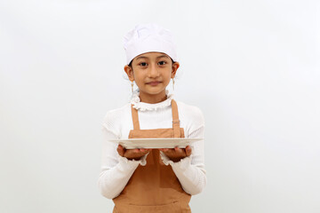 Happy asian little girl in chef uniform smiling while holding empty plate. Isolated on white background