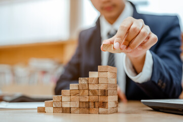 Businessman hand pulling out or placing wood block on the tower and semi-pyramid in modern office....
