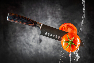 Messer schneidet durch frische Tomate und Wasser läuft runter. - 560190113