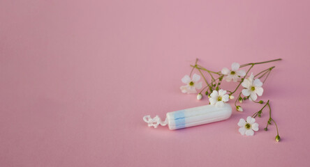 The concept of careful and gentle protection in critical days. Menstruation period concept. Hygienic white tampons for women with flowers on pink backround.