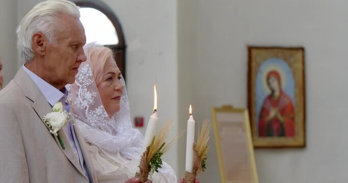 wishing 70 year old couple get married in an orthodox church, holding burning candles in their hands. grandfather and grandmother in churches with candles. 50th anniversary