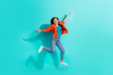 Fototapeta na wymiar Full length photo of funny excited girl dressed orange shirt jumping high arms sides isolated turquoise color background