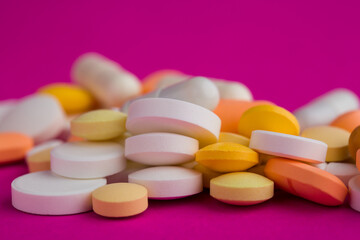 Assorted pharmaceutical medicine pills, tablets and capsules on magenta background.