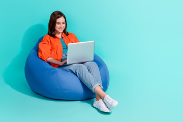 Full length photo of positive girl dressed shirt bean bag writing message device empty space isolated turquoise color background