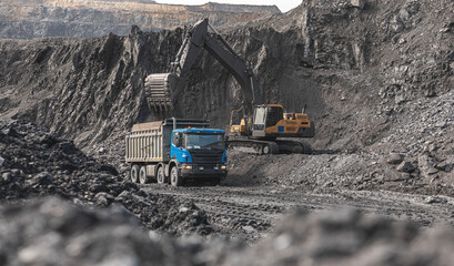 Large quarry dump truck. Big yellow mining truck at work site. Loading coal into body truck. Production useful minerals. Mining truck mining machinery to transport coal from open-pit production - obrazy, fototapety, plakaty