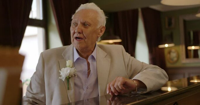 a strange elderly man sits at the bar with his mouth open and turns around. gray-haired hanфdsome old man in a tuxedo. 50th anniversary groom sits at the bar counter.