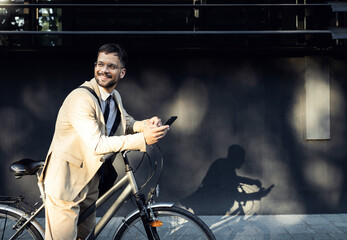 Portrait of business man with bicycle standing in front of office building using smartphone.