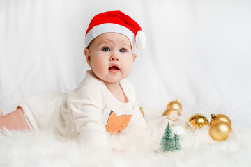 Obraz na płótnie Canvas Cute Christmas little baby in a red Santa hat with Christmas balls on a white background. Christmas and New Year