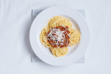 Top view of Bolognese spaghetti with parmesan cheese on top in white plate. Simple white background and decoration. Traditional Italian dish, Mediterranean cuisine. 