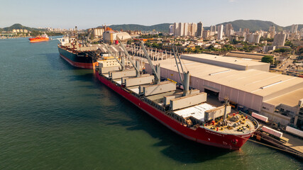 image of red ship with cranes moored at port terminal