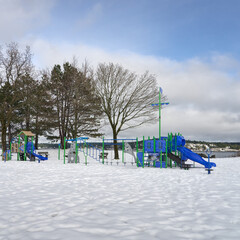 An empty children's playground beside the ocean in a snow covered park on a bright winter day.