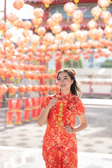Obraz premium Happy Chinese new year. Young asian woman wearing traditional cheongsam qipao dress holding blessing fortune card in Chinese Buddhist temple. Chinese text means blessed by a lucky star. Emotion Smile