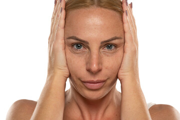 Fototapeta premium Middle aged blond woman tightens her face with her hands on a white background