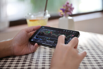 Woman hand using a smartphone for Stock exchange trading online in the coffee shop, business concept