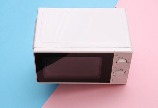 White Microwave oven on a blue-pink pastel background.