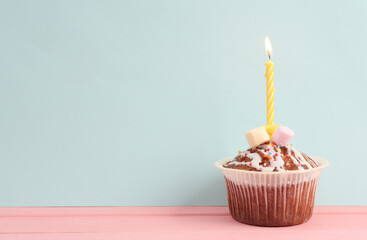 Cupcake with a flaming candle on a pastel background. Birthday concept