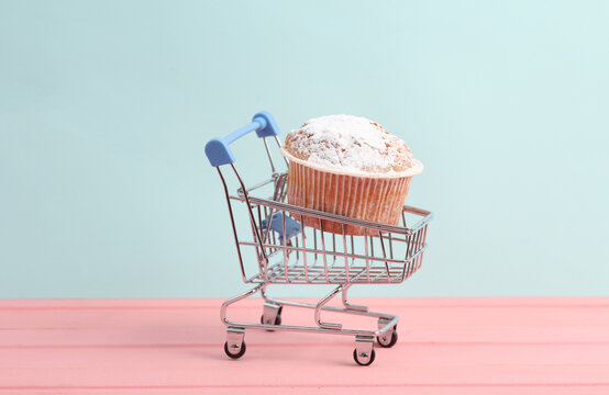 Mini supermarket trolley with appetizing cupcake on a pastel background