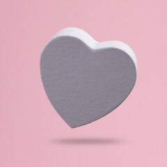 White heart shaped gift box levitating on pink background with shadow