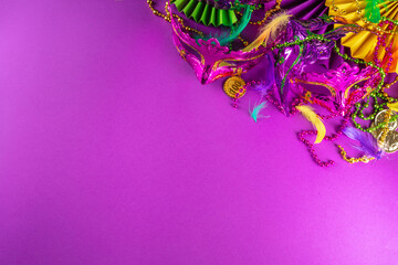 Mardi Gras colourful holiday greeting card background with festival masquerade accessories, decor, carnival mask, beads, feathers, fan on bright background traditional yellow purple green colors