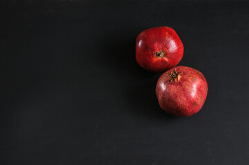 Fototapeta na wymiar Two ripe pomegranates on a black board, top view. Selective focus with copy space, natural light