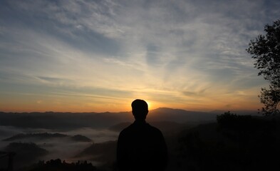 Fototapeta premium A man facing in front of the sun is rising from a back mountain and there has a sea of fog too.