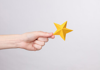Woman's hand holds one paper star on a gray background. Service rating