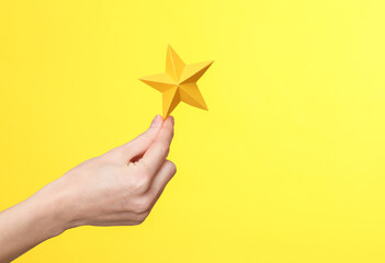 Woman's hand holds one paper star on a yellow background. Service rating