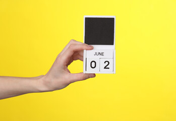 Woman's hand holds wooden calendar with date june 02 on a yellow background