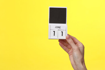 Woman's hand holds wooden calendar with date june 11 on a yellow background