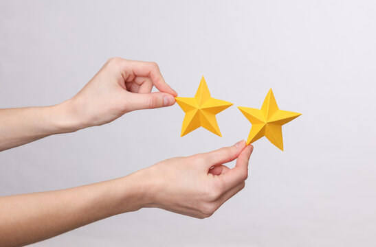 Female hand holds two paper stars on a gray background. Service rating