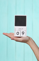 Woman's hand holds wooden calendar with date july 09 on blue wooden background